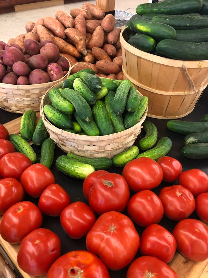Colorful assortment of fresh vegetables including tomatoes, cucumbers, and sweet potatoes at a market.
