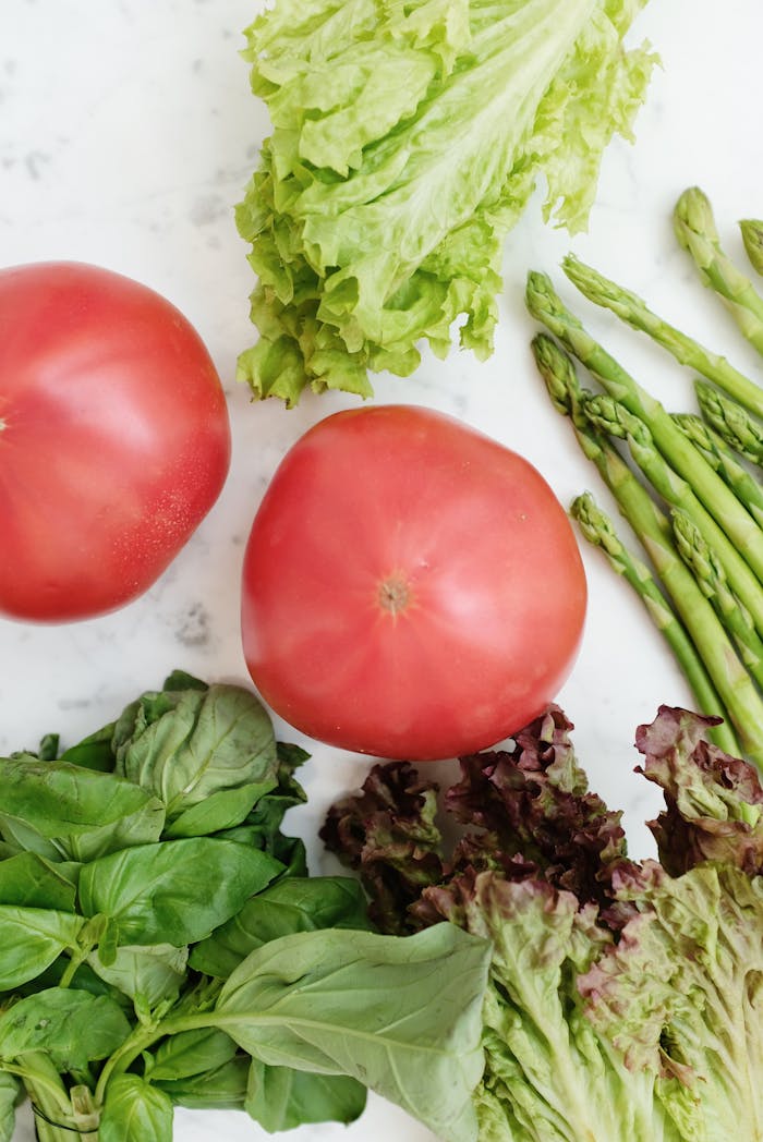 Vibrant assortment of fresh vegetables, including tomatoes, lettuce, and asparagus on a white background.